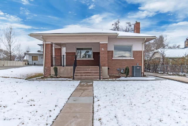 view of front of house with central air condition unit, fence, covered porch, brick siding, and a chimney