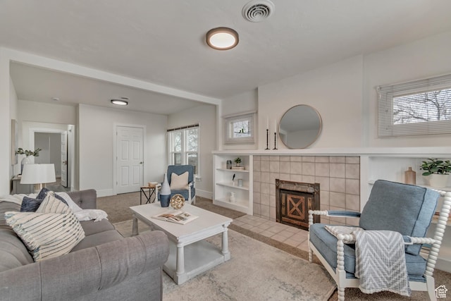 living area featuring plenty of natural light, visible vents, a tile fireplace, and carpet