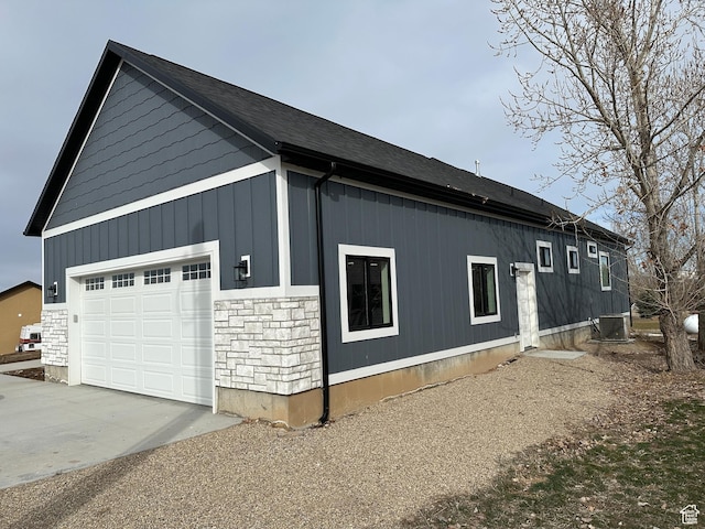 view of side of property featuring central AC unit, concrete driveway, and stone siding