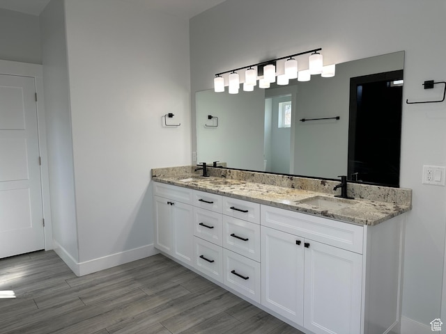bathroom featuring baseboards, wood finished floors, double vanity, and a sink