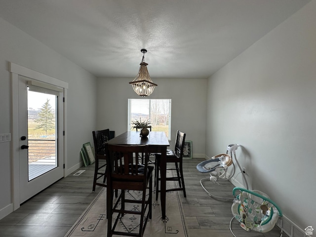 dining area featuring a notable chandelier, baseboards, wood finished floors, and visible vents
