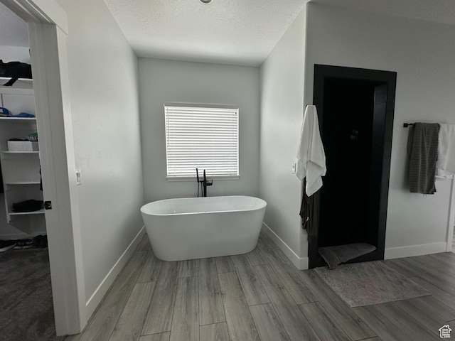 full bathroom featuring a textured ceiling, a freestanding tub, wood finished floors, and baseboards
