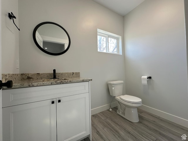 bathroom with toilet, wood finished floors, vanity, and baseboards