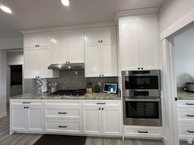 kitchen with white cabinets, appliances with stainless steel finishes, light stone countertops, and under cabinet range hood