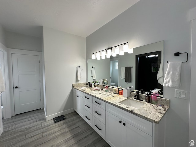 full bath featuring a sink, double vanity, baseboards, toilet, and wood finished floors