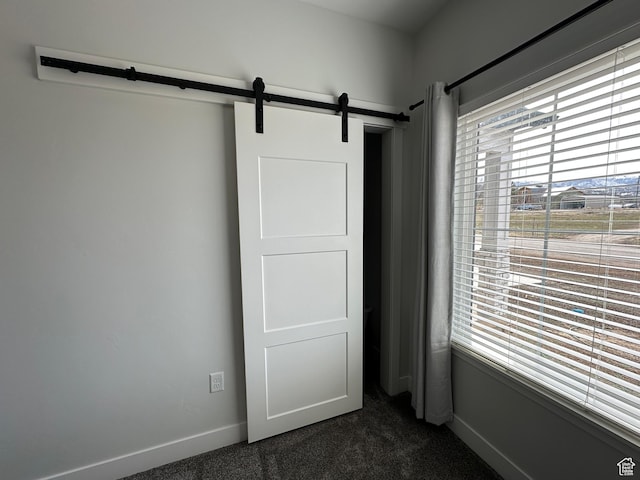 unfurnished bedroom with dark colored carpet, a barn door, and baseboards