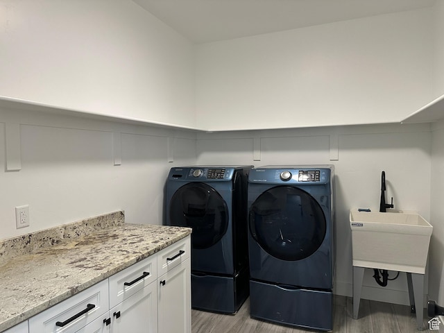 clothes washing area featuring light wood-type flooring, cabinet space, washing machine and clothes dryer, and a decorative wall