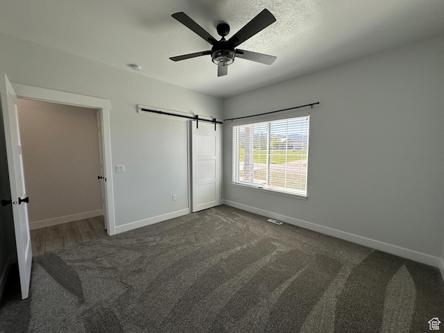 unfurnished bedroom featuring a closet, carpet flooring, a barn door, and baseboards