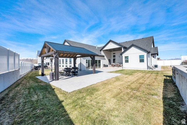 rear view of property with a lawn, a fenced backyard, board and batten siding, metal roof, and a patio area