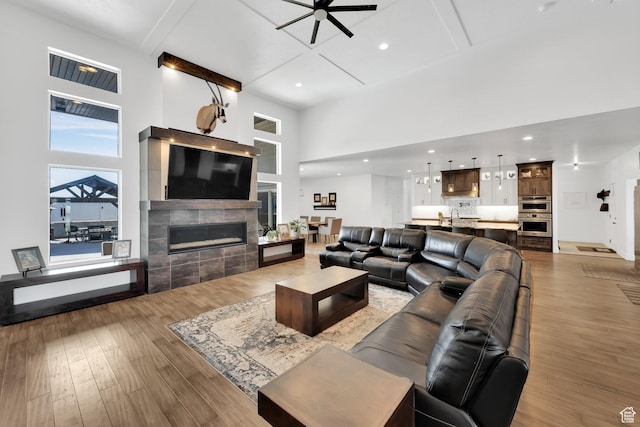 living area featuring wood finished floors, a ceiling fan, beam ceiling, a high ceiling, and a tiled fireplace