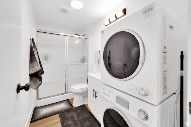 bathroom with visible vents, stacked washer and dryer, toilet, wood finished floors, and a shower stall