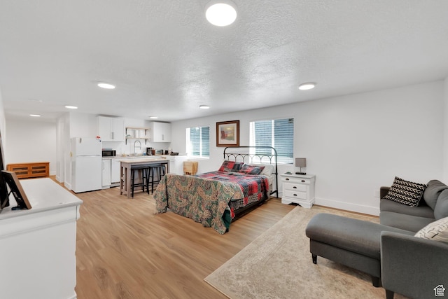 bedroom with a textured ceiling, light wood-type flooring, freestanding refrigerator, and a sink