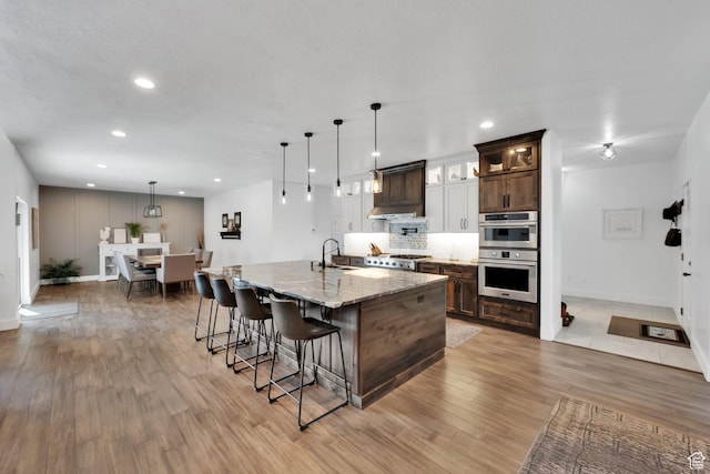 kitchen featuring a breakfast bar, double oven, light wood-type flooring, and decorative backsplash