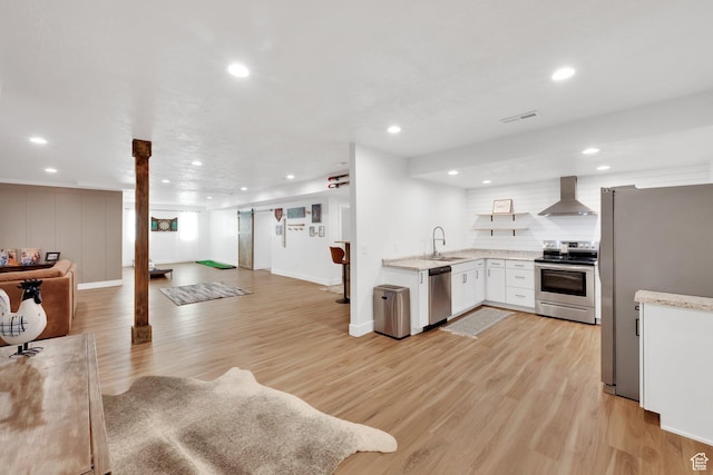 kitchen with visible vents, open floor plan, appliances with stainless steel finishes, wall chimney exhaust hood, and a sink