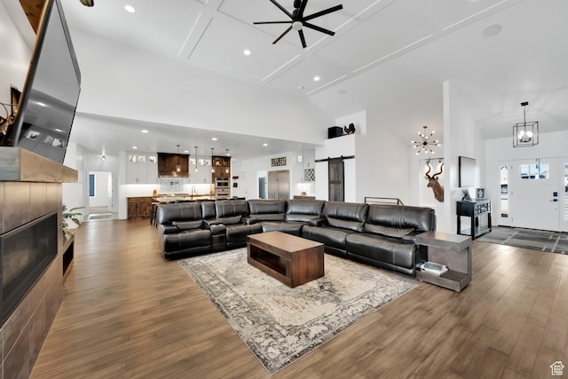 living area featuring a tiled fireplace, a barn door, a high ceiling, and dark wood-style flooring