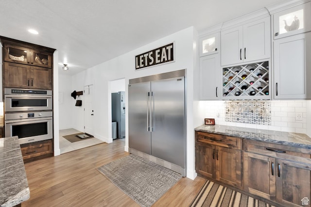 kitchen featuring stainless steel appliances, light stone countertops, light wood-style floors, and decorative backsplash