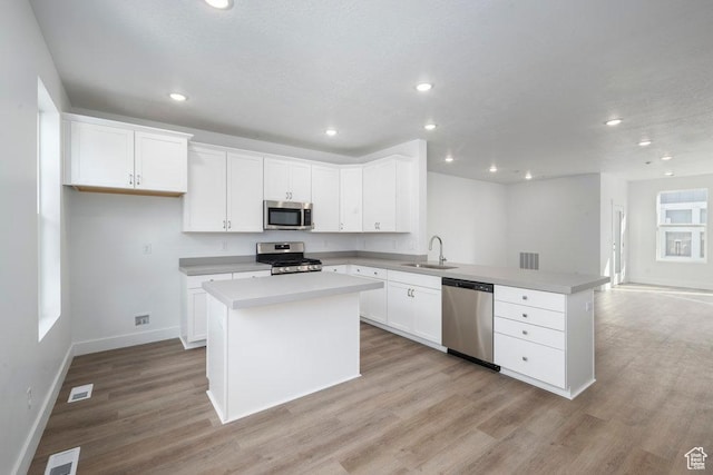 kitchen with a peninsula, light wood-style flooring, a sink, light countertops, and appliances with stainless steel finishes
