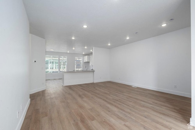 unfurnished living room featuring light wood finished floors, recessed lighting, baseboards, and a sink