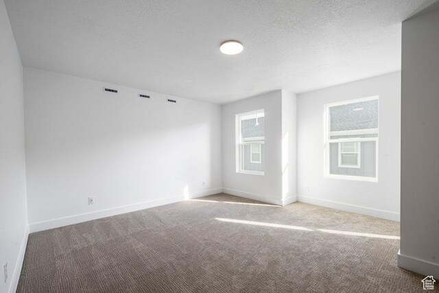 spare room with carpet flooring, visible vents, baseboards, and a textured ceiling