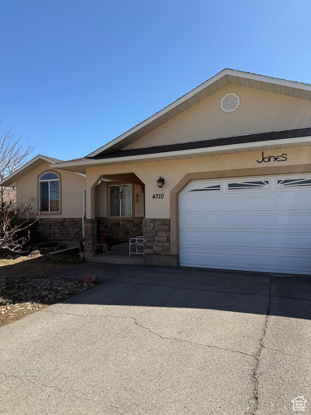 single story home with concrete driveway, an attached garage, stone siding, and stucco siding