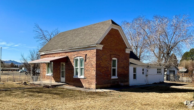 view of side of property with fence, brick siding, roof with shingles, and a lawn