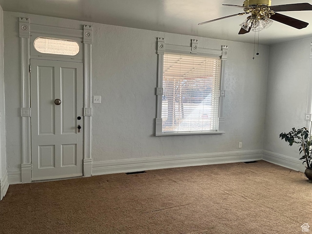 carpeted foyer entrance with visible vents, baseboards, a ceiling fan, and a textured wall