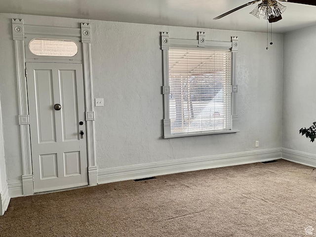 foyer with visible vents, carpet, baseboards, ceiling fan, and a textured wall