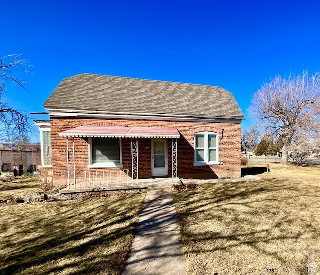 bungalow-style house with brick siding, a front yard, and roof with shingles