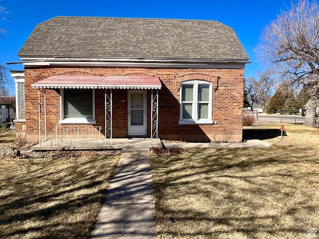 view of front facade with a front yard, brick siding, and a shingled roof