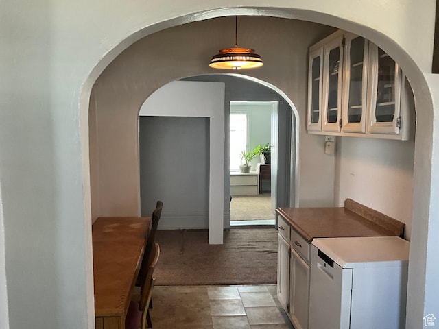 kitchen with light carpet, pendant lighting, white cabinetry, light countertops, and glass insert cabinets