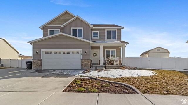 view of front of home featuring stone siding, a porch, concrete driveway, and fence