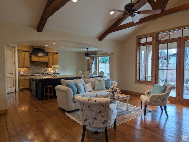 living room with vaulted ceiling with beams, arched walkways, ceiling fan, dark wood-style flooring, and baseboards