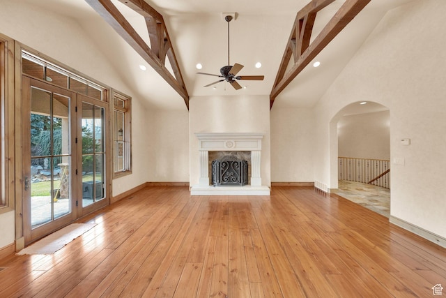 unfurnished living room with high vaulted ceiling, ceiling fan, light wood-style flooring, baseboards, and arched walkways