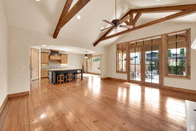 unfurnished living room with ceiling fan, plenty of natural light, beamed ceiling, and baseboards