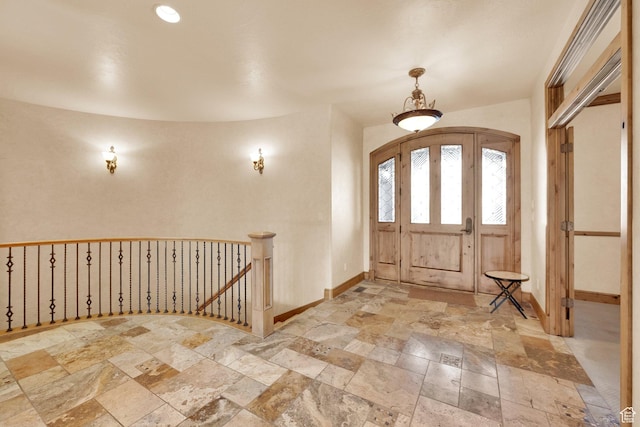 foyer featuring arched walkways, stone tile floors, and baseboards