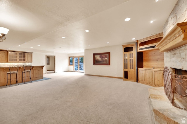unfurnished living room with light colored carpet, recessed lighting, a stone fireplace, and baseboards
