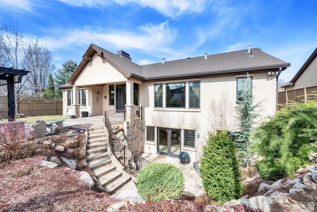 rear view of house with stairway, a chimney, stucco siding, french doors, and fence