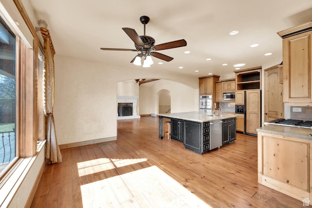 kitchen featuring ceiling fan, open shelves, a center island with sink, arched walkways, and appliances with stainless steel finishes