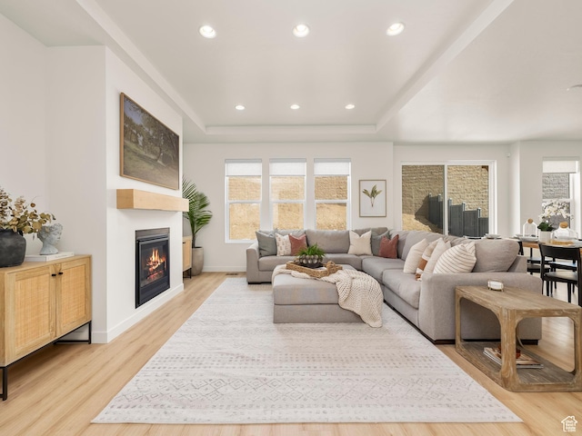 living room with a raised ceiling, a glass covered fireplace, recessed lighting, light wood finished floors, and baseboards