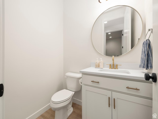 half bath with toilet, vanity, baseboards, and wood finished floors
