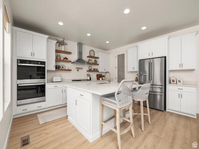 kitchen with visible vents, wall chimney range hood, stainless steel fridge with ice dispenser, double wall oven, and open shelves