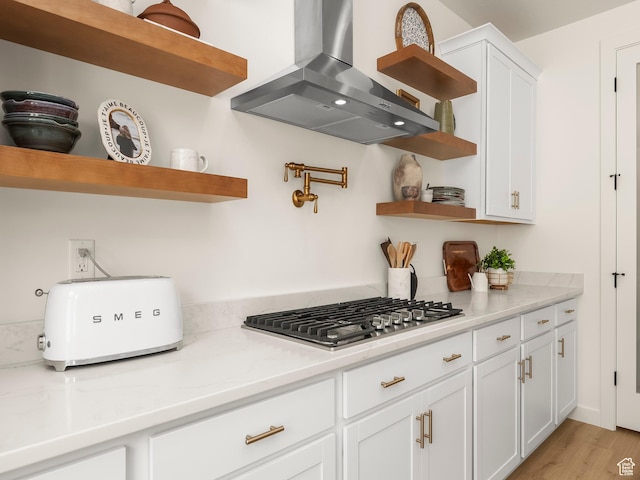 kitchen with wall chimney range hood, light countertops, stainless steel gas stovetop, white cabinetry, and open shelves