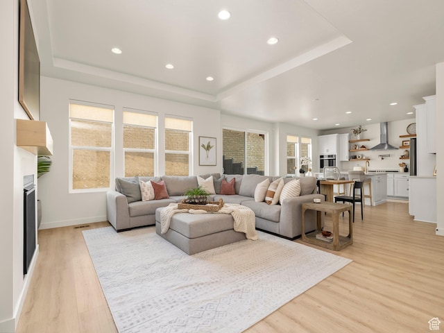 living area with recessed lighting, light wood-type flooring, a raised ceiling, and a fireplace