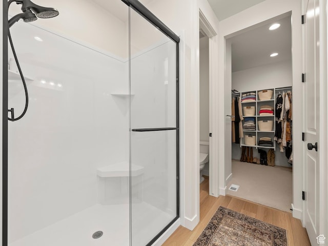 full bath featuring a shower stall, a walk in closet, toilet, recessed lighting, and wood finished floors