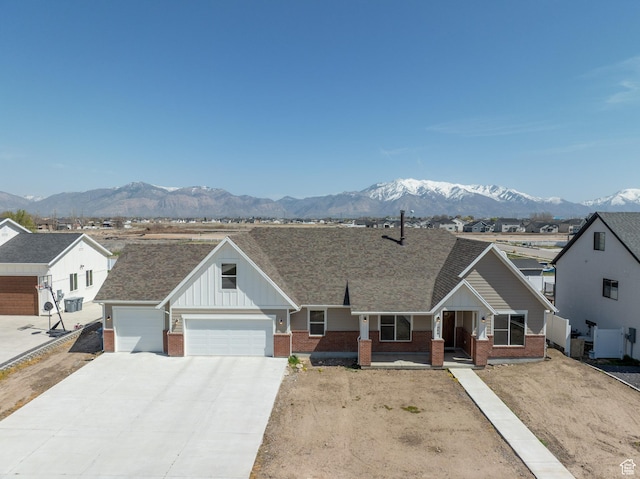 ranch-style house with board and batten siding, a garage, brick siding, a mountain view, and concrete driveway