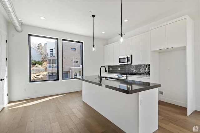 kitchen featuring wood finished floors, a sink, stainless steel appliances, dark countertops, and tasteful backsplash