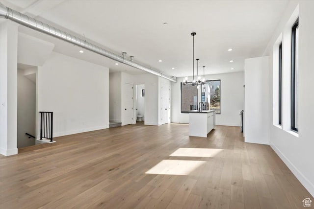 unfurnished living room with light wood finished floors, baseboards, recessed lighting, an inviting chandelier, and a sink