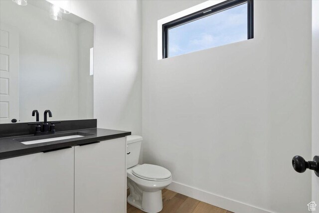 half bathroom featuring vanity, toilet, wood finished floors, and baseboards