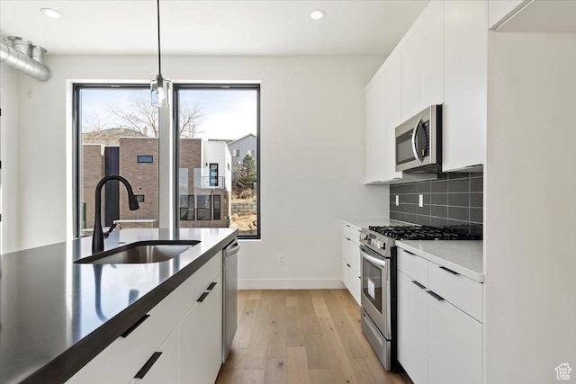 kitchen with light wood-type flooring, a sink, backsplash, white cabinetry, and appliances with stainless steel finishes