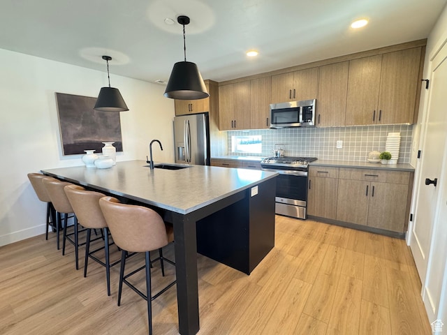 kitchen featuring a sink, stainless steel appliances, a kitchen bar, light wood-type flooring, and backsplash